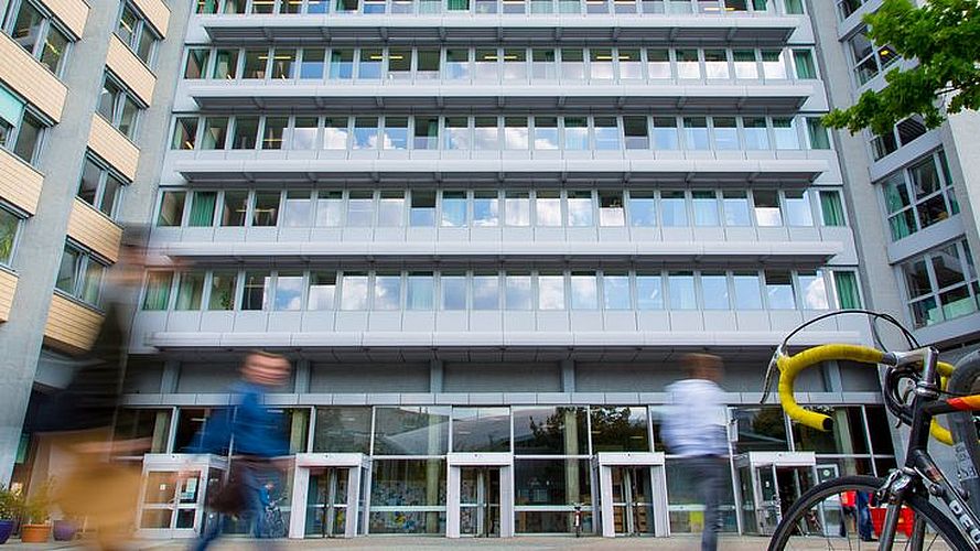 Eingangsbereich des Philosophenturms der Uni Hamburg, davor sind verwischt Menschen in Bewegung und mit Rad zu sehen